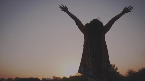 silhouette of hippie woman with dreadlocks raising arms to sky