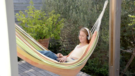 relaxing in hammock, woman listening to music with headphones and using tablet