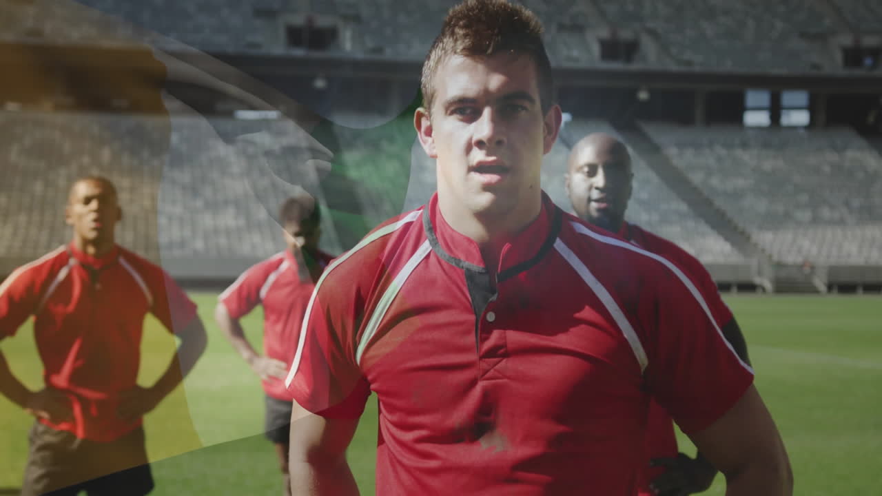 Standing on field, rugby players in red jerseys with stadium in background