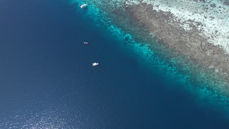 flying towards beautiful coral reefs with dingies waiting for divers next to mioskon island with white sandy beach in raja ampat, indonesia, papua