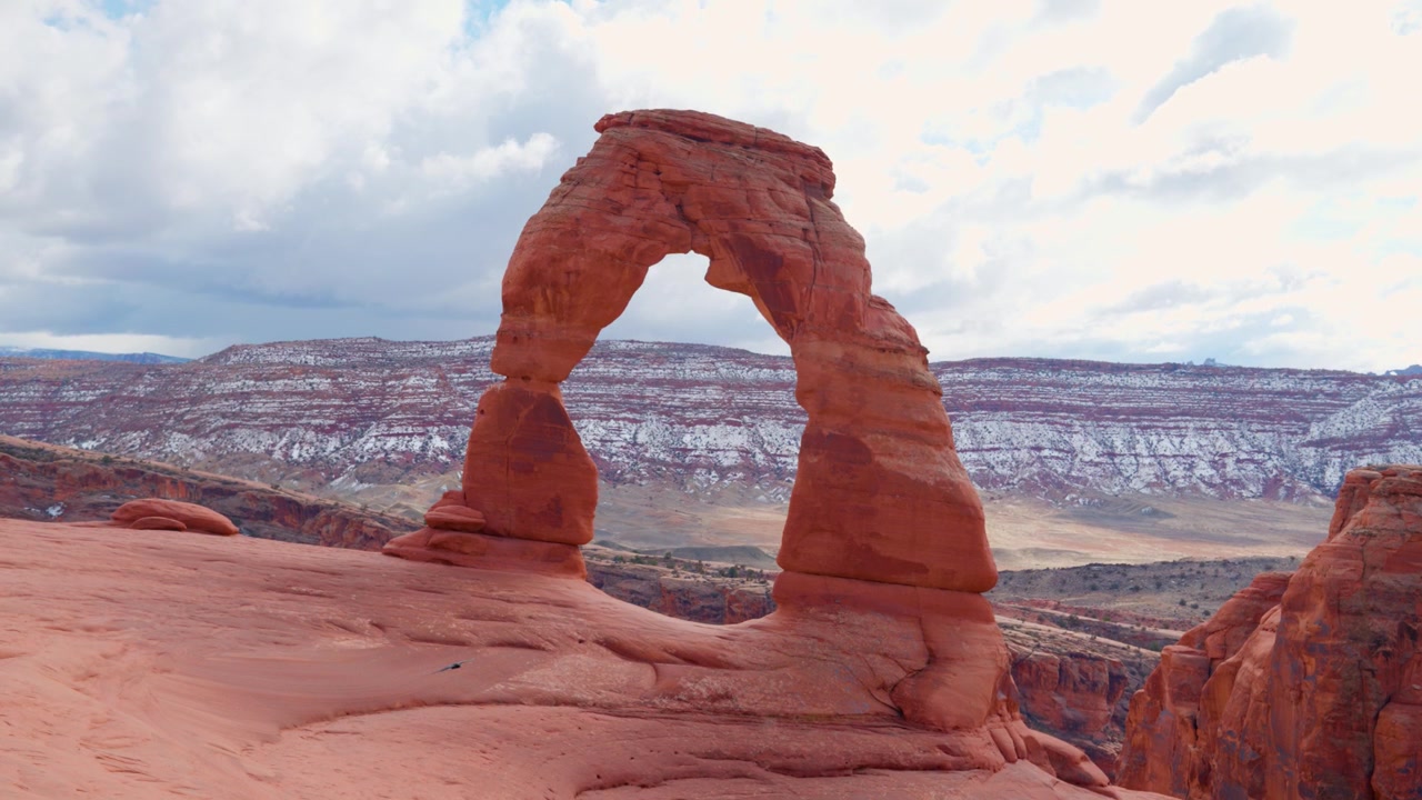 Pengambilan gambar lebar statis Delicate Arch di Taman Nasional Arches pada hari yang cerah dan berawan indah dengan seekor gagak terbang di latar belakang