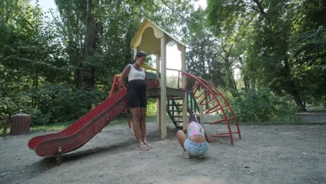 pregnant mother watching daughter play on slide at playground