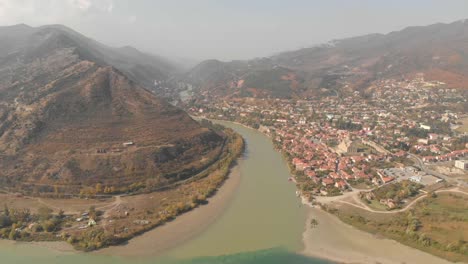 Flying-over-a-fork-in-the-river-towards-the-city-of-Mtskheta,-Georgia,-tucked-into-a-mountain-valley-hillside