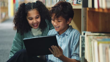 two children reading a tablet in a library