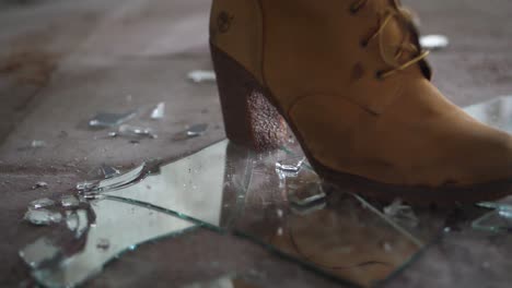 a close up shot a woman with a pair of suede brown boots, kicking down on a piece of mirror, cracking and destroying the glass into small pieces