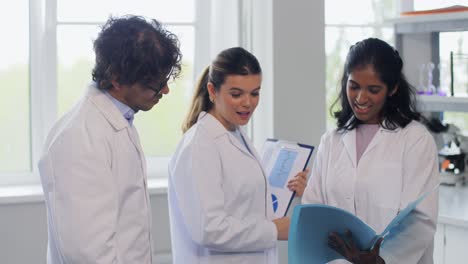 International-Group-of-Scientists-in-Laboratory.science-research,-work-and-people-concept-international-group-of-happy-scientists-with-clipboards-discussing-report-in-laboratory