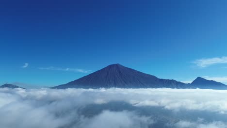 stunning drone footage of mount rinjani, lombok, with the majestic mountain peeking through the clouds, showcasing the island's natural beauty.