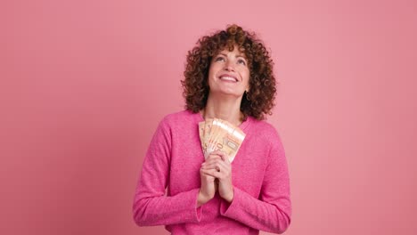 cheerful woman showing euro banknotes in pink studio