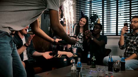 multiethnic friends congratulate caucasian shy birthday girl with sparkling firework cake at surprise party slow motion