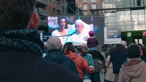 pope francis addresses a large crowd on a public screen
