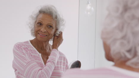 mujer mayor mirando el reflejo en el espejo del baño cepillando el cabello