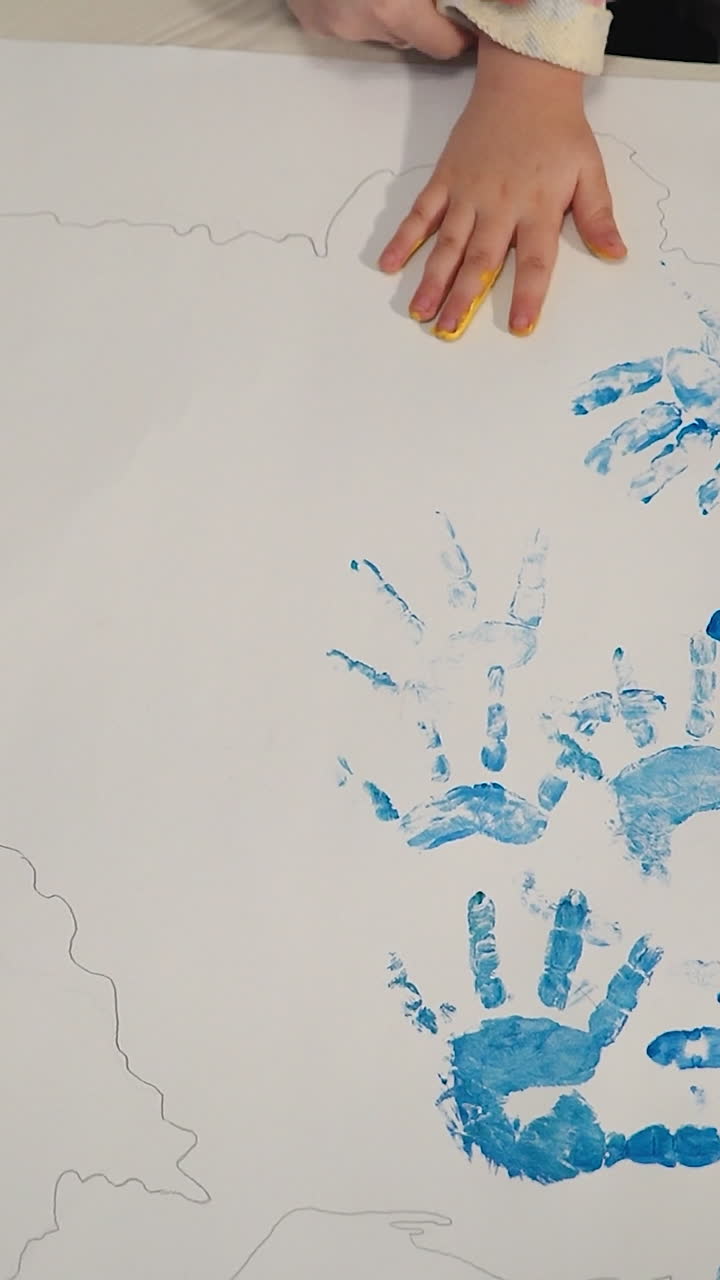 Child making hand print on paper. ?olorful designs with hands. Little painter. Vertical video