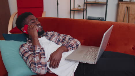 Young-man-using-laptop-computer-sitting-on-sofa-working,-online-shopping-from-home-office