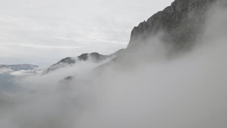 Rocky-mountain-range-standing-above-dense-cloudscape,-aerial-drone-view-while-fly-through-clouds