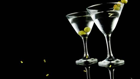 Golden-confetti-falling-over-olives-in-two-cocktail-glasses-against-black-background