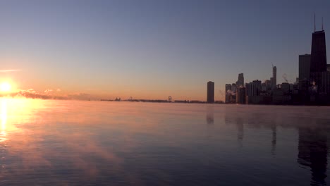 Sol-Saliendo-Sobre-El-Horizonte-Del-Lago-Michigan-Sobre-El-Horizonte-Del-Centro-De-Chicago-En-Invierno-Con-Humo-De-Mar-En-El-Agua-Durante-El-Vórtice-Polar-4k