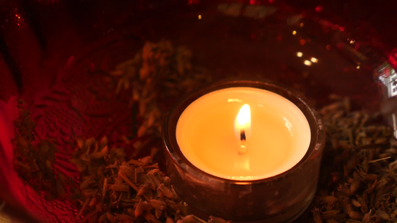 A single lit candle in a glass holder with a red background.
