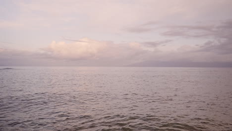 Overview-of-ocean-waves-washing-on-a-sandy-beach-after-sunset-with-mountain-silhouette-in-the-background