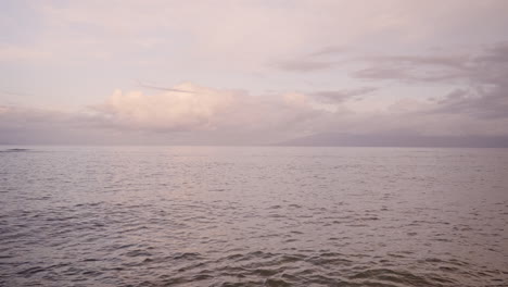 overview of ocean waves washing on a sandy beach after sunset with mountain silhouette in the background