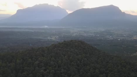 Aerial-Flying-Over-Tropical-Forest-Hill-With-View-Of-Doi-Luang-Chiang-Dao-Mountains-In-Background-During-Golden-Hour