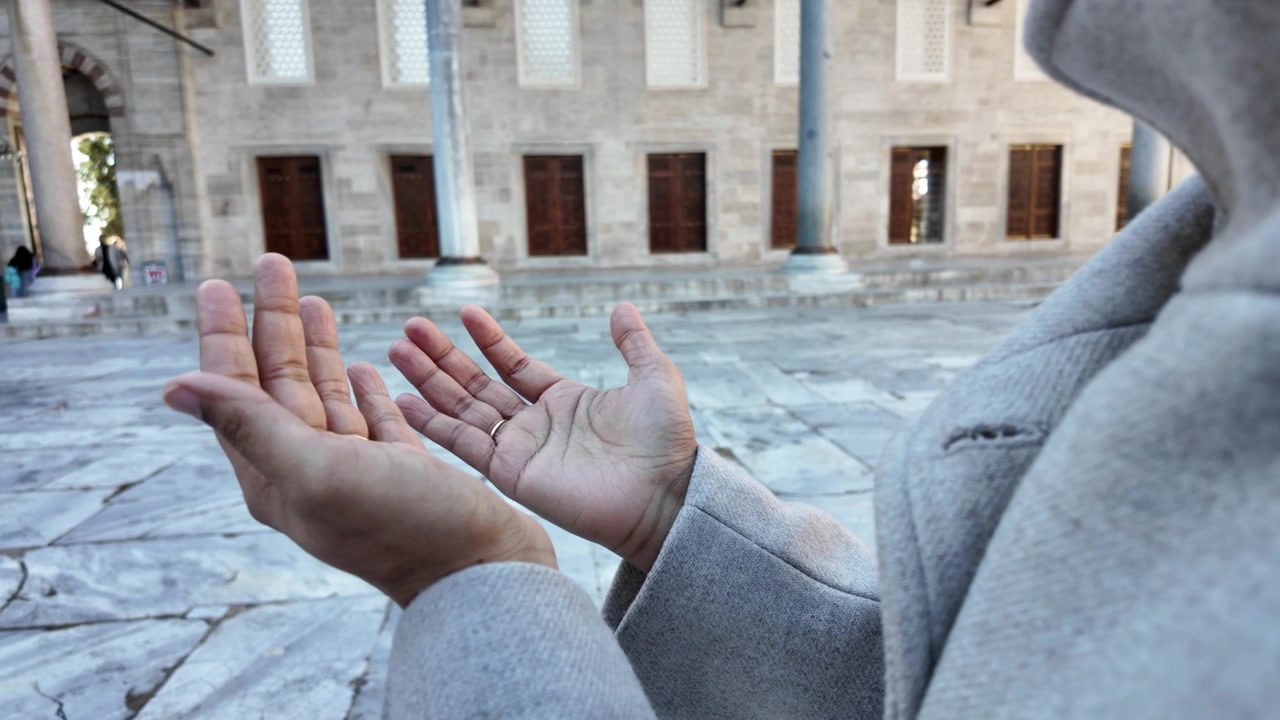 Tarihi caminin önünde elleri açık dua eden kişi