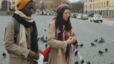 multiethnic couple feeding pigeons on town square