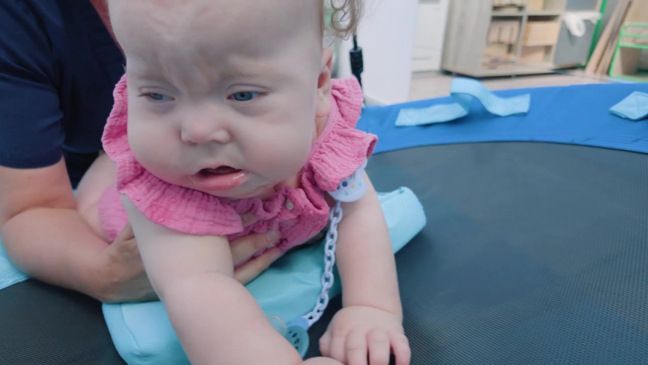 Close-up of a baby girl with a fussy expression, held by an adult