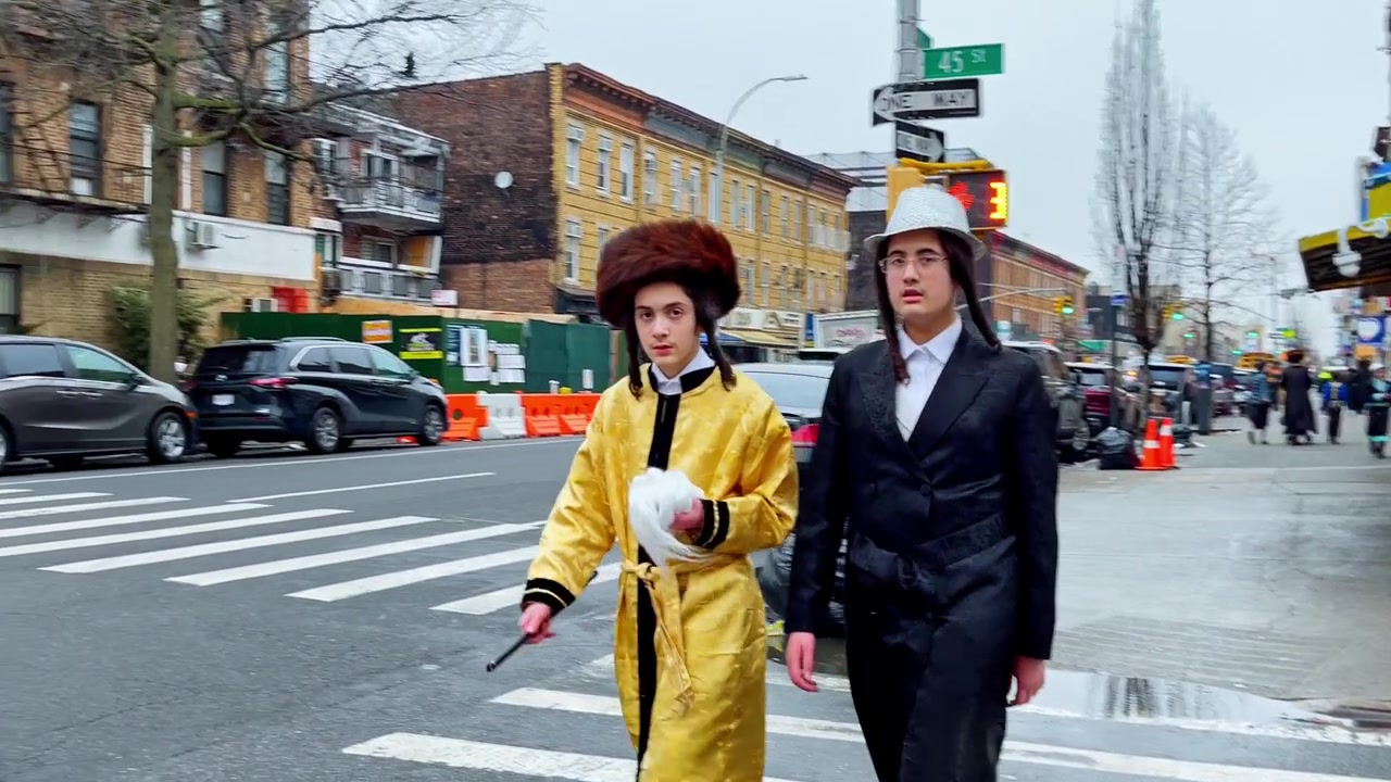 New York, USA, 9 March 2022: Hasidic boys in Purim costumes on Brooklyn sidewalk. Two Hasidic boys in traditional clothing and Purim costume walk near 43 St, overcast daylight.
