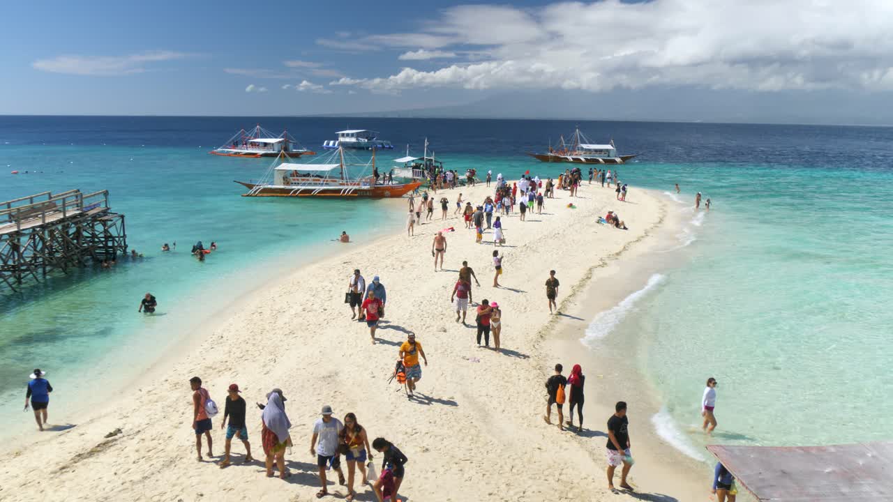 Tourists walking along a sandbar surrounded by crystal clear waters in Sumilon Island, Cebu