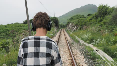 persona caminando por las vías del tren con auriculares puestos