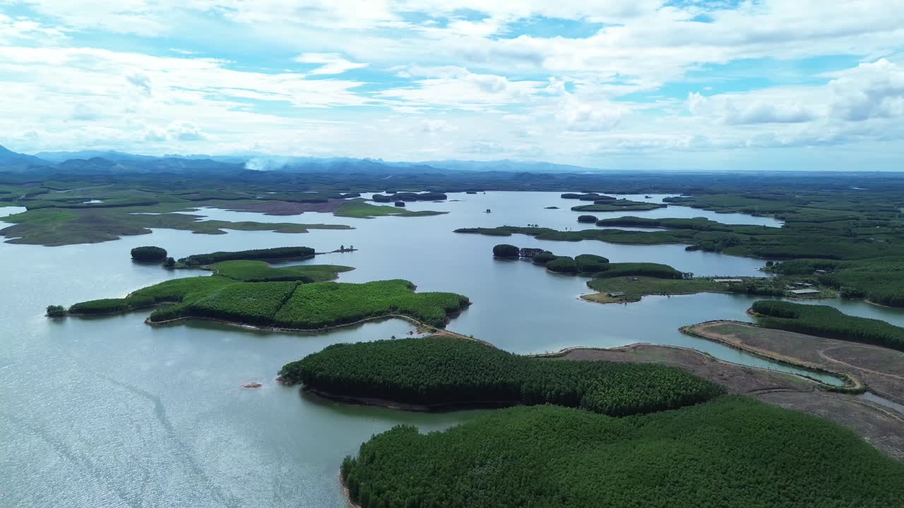 Smooth aerial zoom out of green islands in lake with forested shoreline and mountains in background