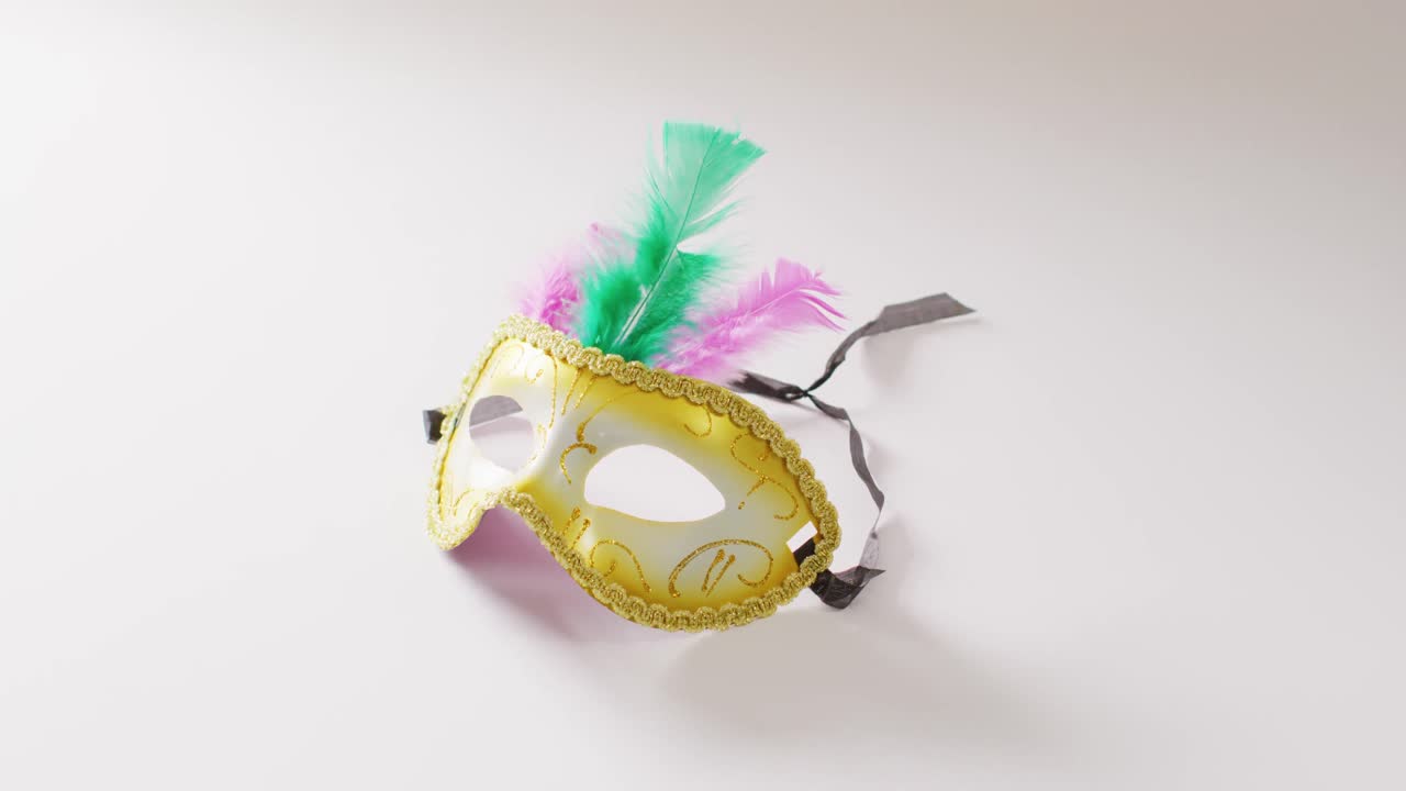 video de una máscara de carnaval de mascarada blanca y dorada con plumas verdes y rosadas sobre fondo blanco