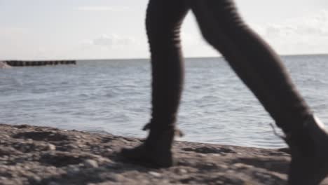 Back-View-Of-A-Woman-Feet-Walking-Along-The-Lake-Shore-During-Sunny-Day-With-Waves-Splashing-the-Shore---Close-Up-Shot