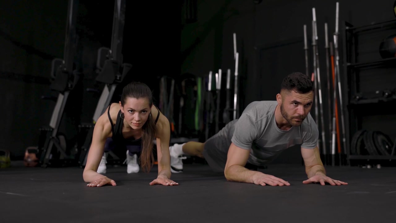 Coppia atletica in posizione plank in una palestra buia
