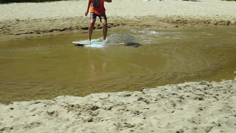 slow motion, a young man is skimming on the beach, there is a beach and a natural climate around