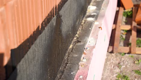 bitumen waterproofing applied to foundation base along red brick wall exterior