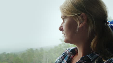 a woman looks out the window of a bus to a forest covered with thick fog traveling in norway