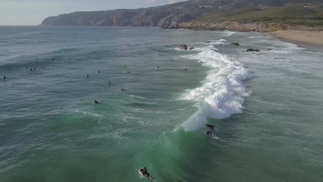 aerial, pan drone shot following surfers on the waves of the atlantic ocean, on a partly sunny evening, at the coast of cascais, in portugal