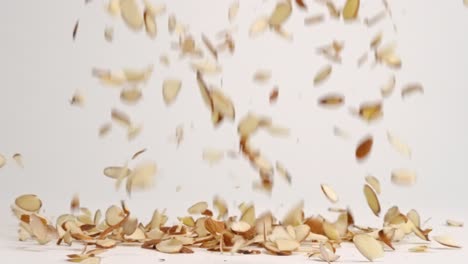 sliced raw brown almond nut pieces falling and bouncing into pile on white table top in slow motion