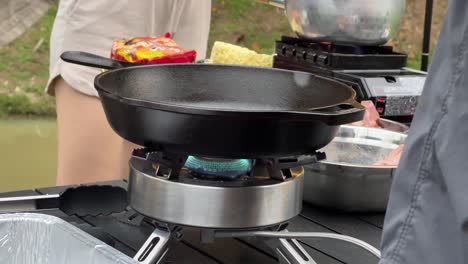 heating up the cast iron pan, chef placing his hand above the pan, making sure it is hot and ready to cook the steaks, outdoor glamping environment