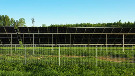 Low-angle-shot-of-solar-panels-farm-from-rear-view,-installed-on-grass-field-at-sunset