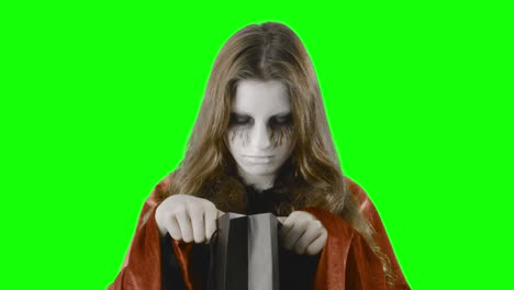 comprobando las golosinas - chica adolescente, disfrazada para halloween o una fiesta de disfraces, contra una pantalla verde