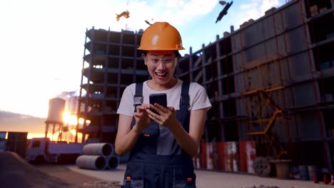 asian woman worker wearing goggles and safety helmet looking at smartphone then screaming goal celebrating while standing at construction site
