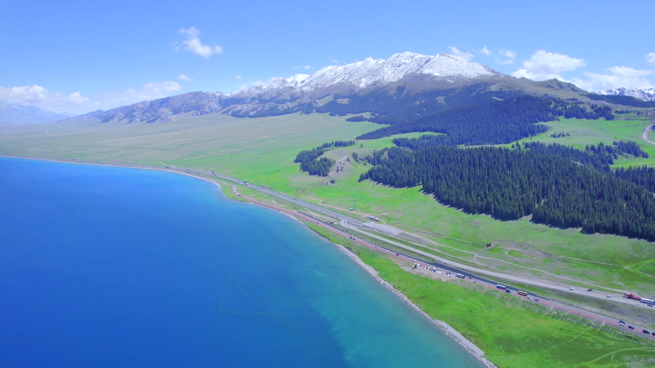 Luftfoto af Sayram-søen i Yili, Xinjiang med Tianshan-snebjergene. Yachtsejlads på alpesø omgivet af nåleskov og græsland. Nordvestkinas naturlandskab ved Sayram-søen.