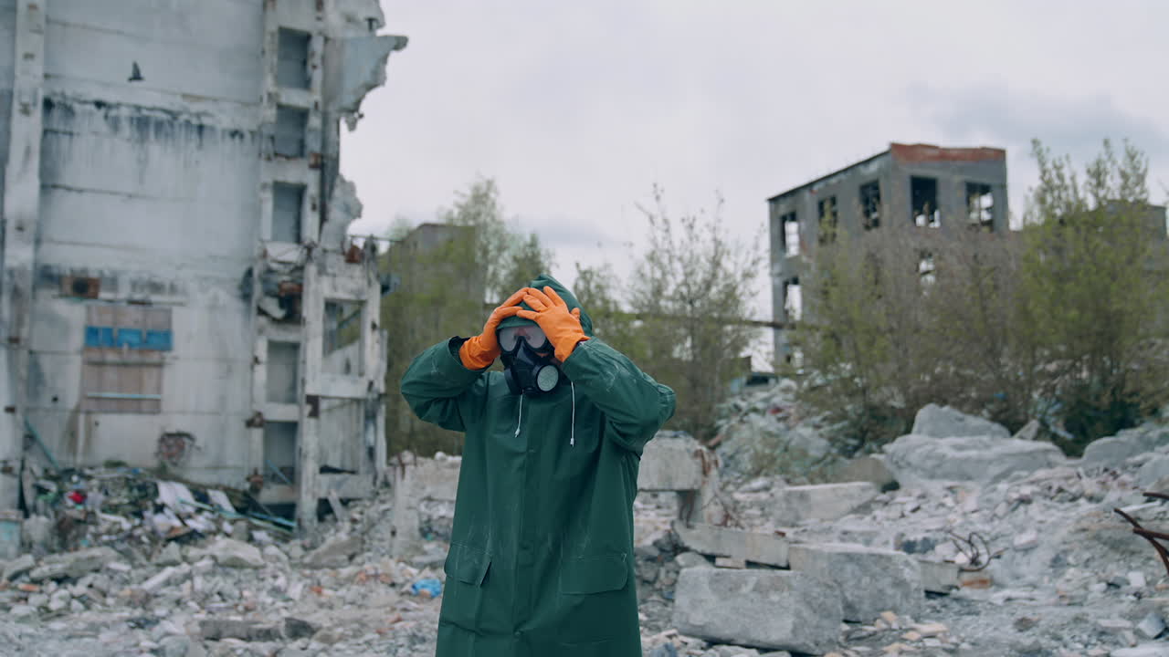 Im shocked. Ecologist in safety suit touching to his head on ruined building background. Person in gas mask and protective clothes stands in dangerous place after chemical attack