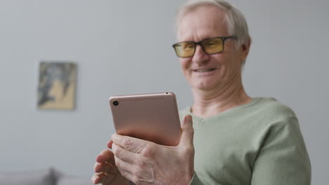 un anciano sonriente que usa una tableta mientras se sienta en una sala de estar moderna en casa