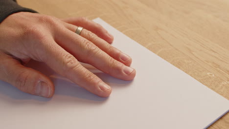 close-up of a man's hand on a white paper on a wooden table