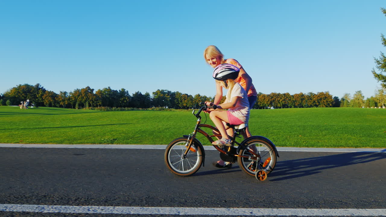 엄마는 소녀에게 자전거 개념을 타도록 가르칩니다 - 행복한 어린 시절 부모를 위한 도움과 지원