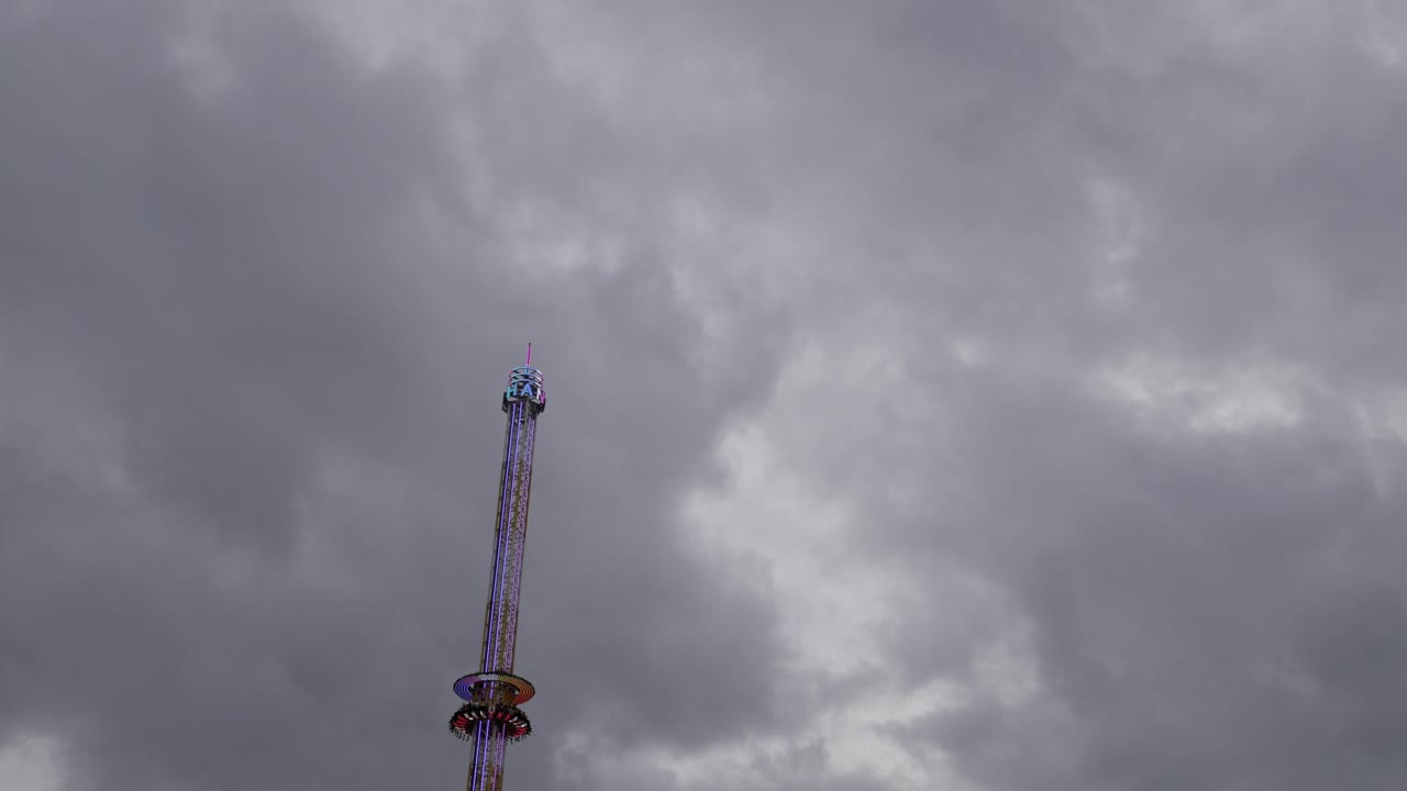 A tall drop tower against a cloudy, dramatic sky, evoking thrill and suspense