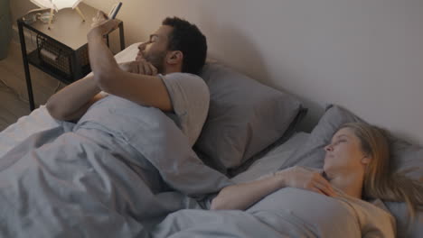 Couple in Bed, One Texting, One Sleeping